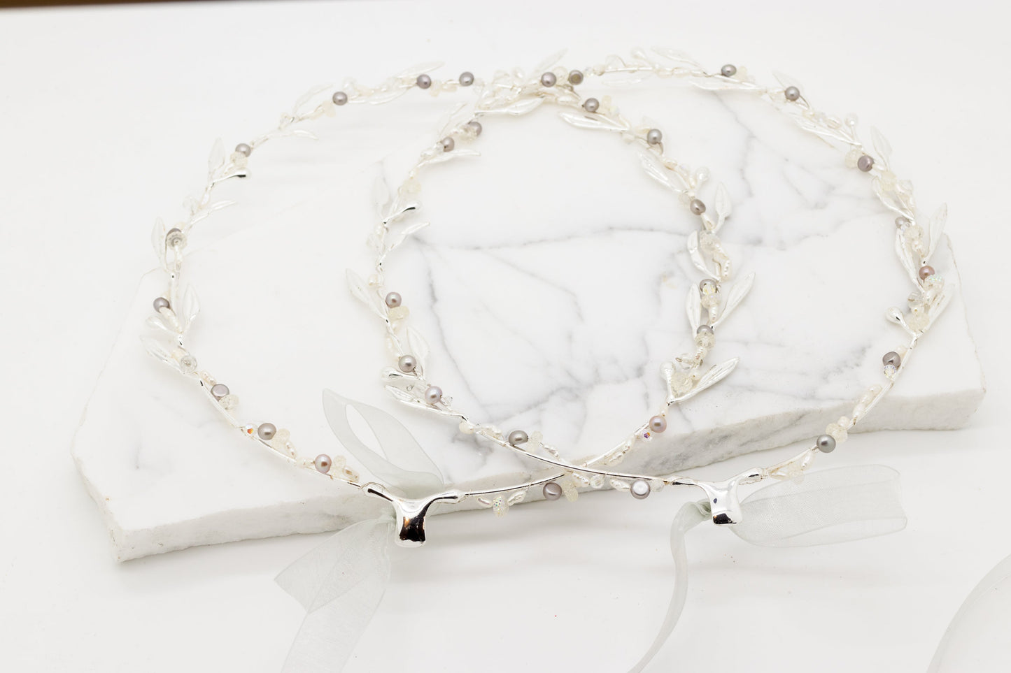 Pair of silver-toned wedding crowns adorned with delicate branches and small pearls.
