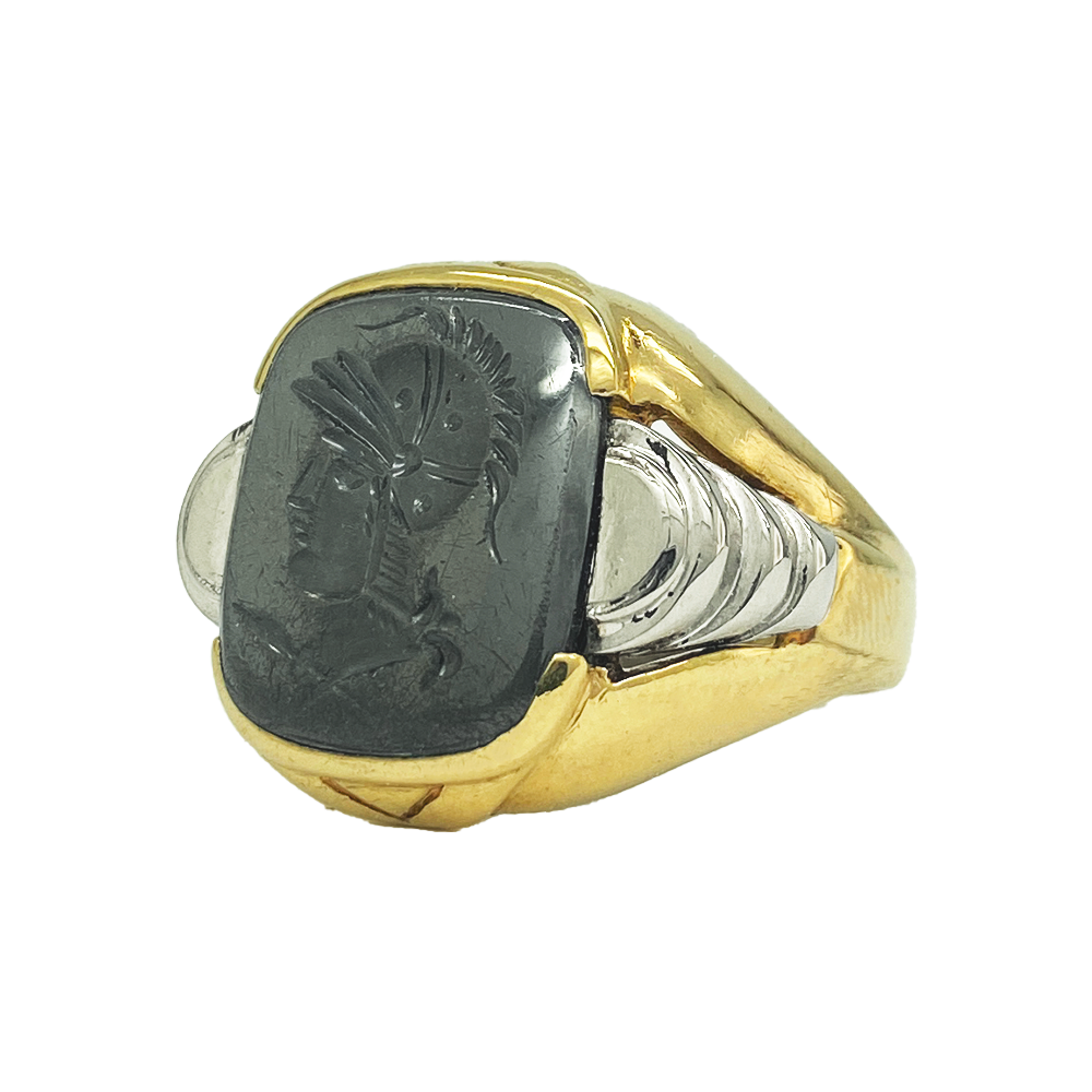 Vintage gold men's ring with a rectangular hematite intaglio featuring a detailed profile of a helmeted warrior. The ring has a textured gold band with a contrasting white metal inlay.