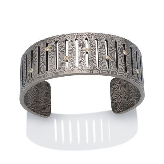 Silver cuff bracelet with Damascus steel pattern on a white background.