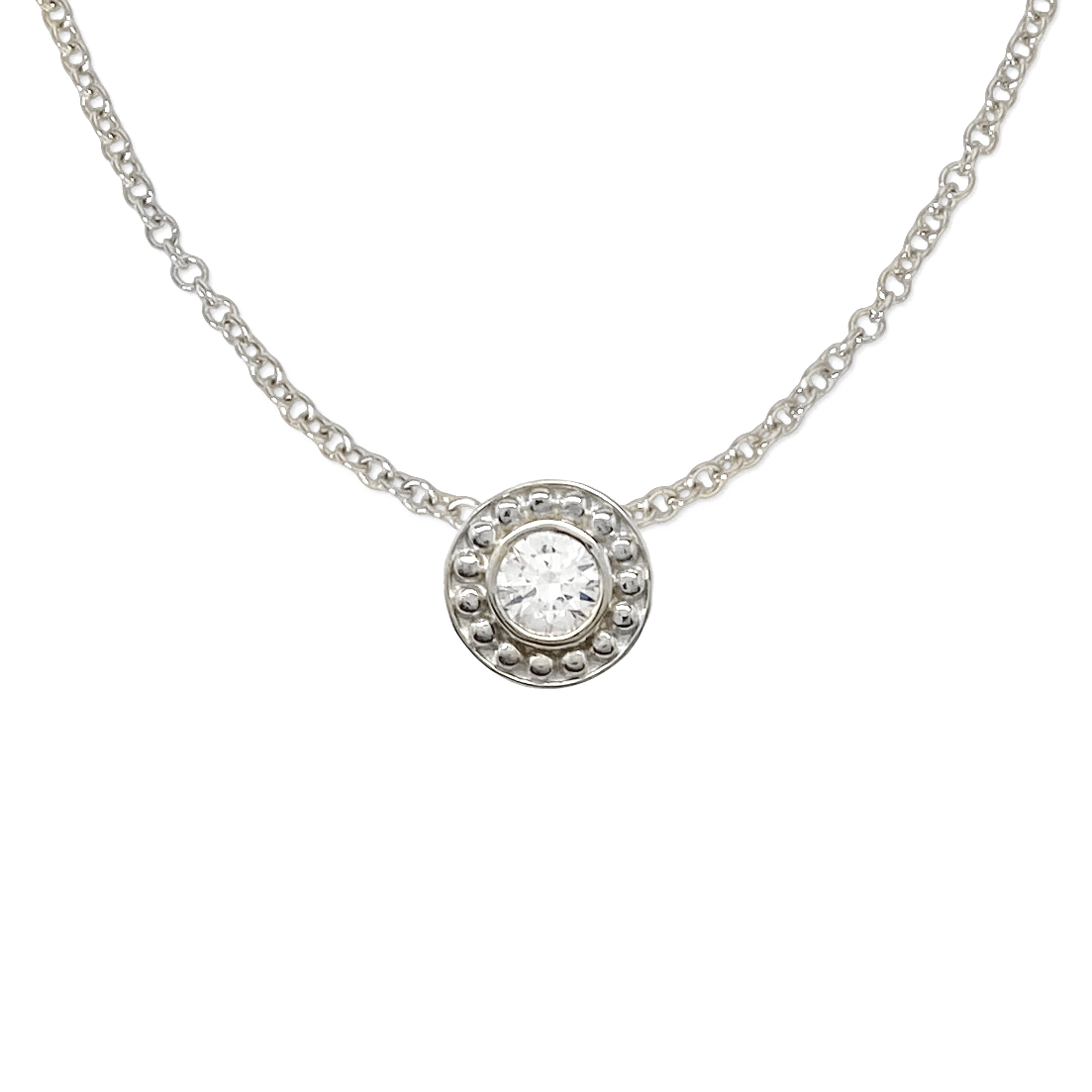 Silver necklace with a circular pendant featuring a diamond surrounded by a beaded border. The background is white.