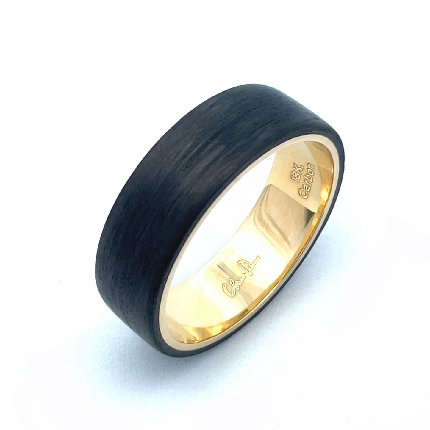 Yellow gold ring with a black carbon fiber inlay on a white background.