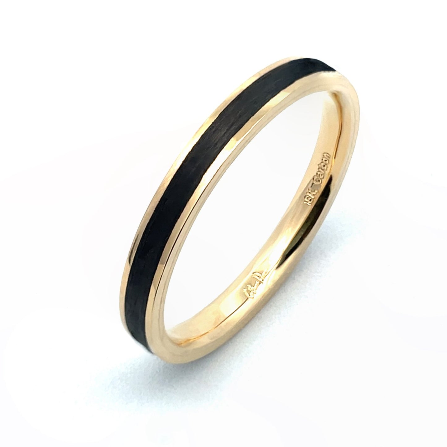 Yellow gold ring with a black carbon fiber inlay on a white background.