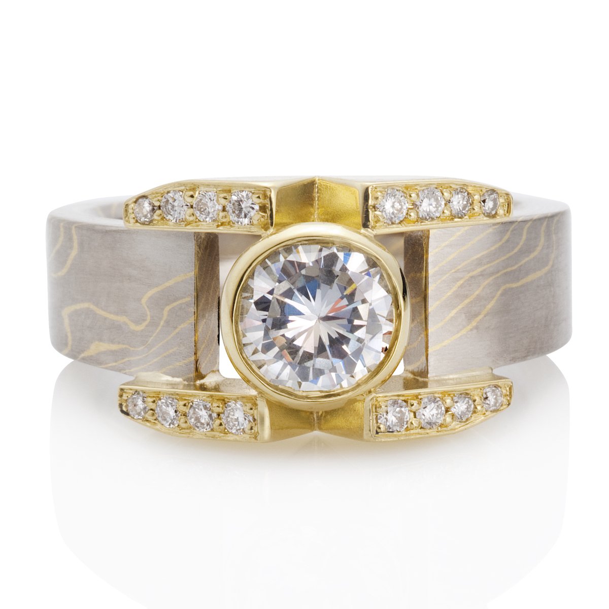 Yellow gold ring with a round diamond center stone, diamond accents, and a Damascus steel band on a white background.