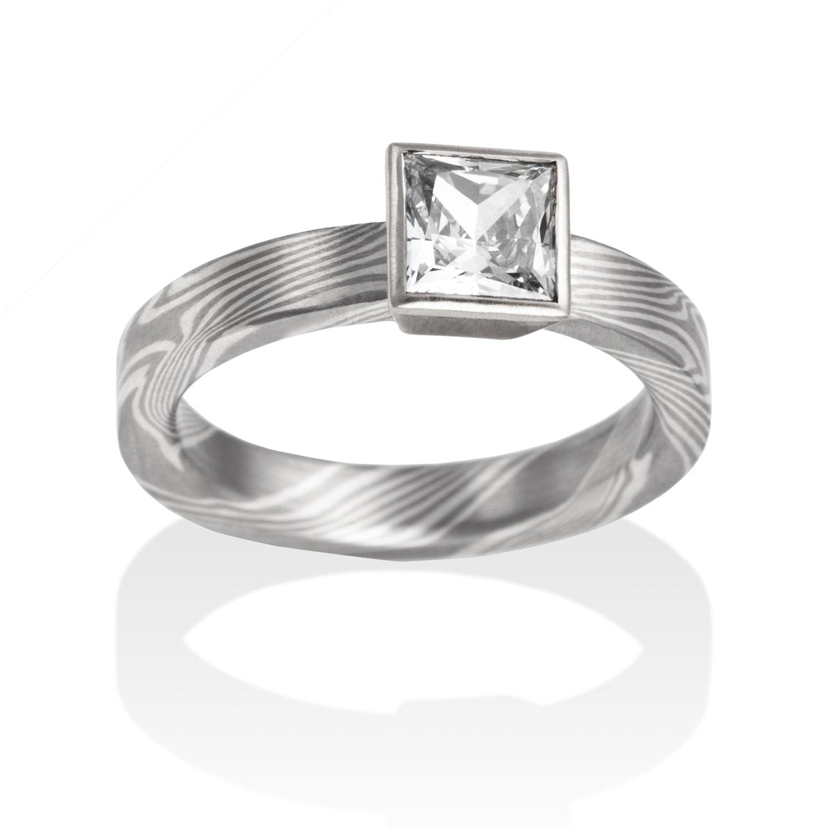 Silver ring with a princess-cut diamond and a Damascus steel band on a white background.