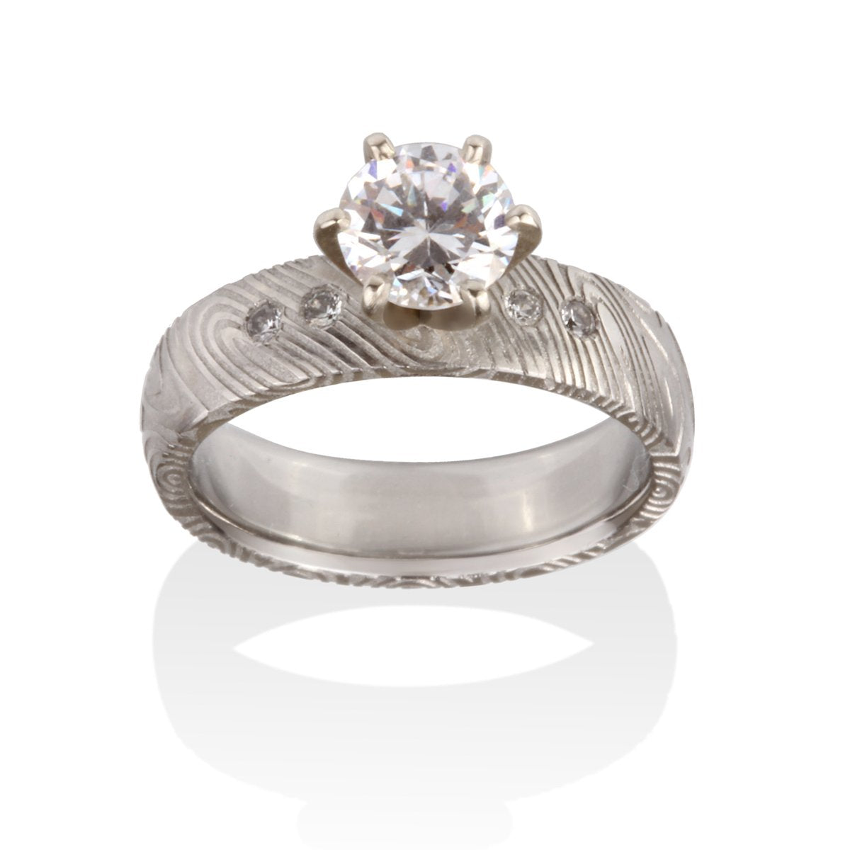 Silver engagement ring with a round diamond center stone, diamond accents, and a Damascus steel band on a white background.