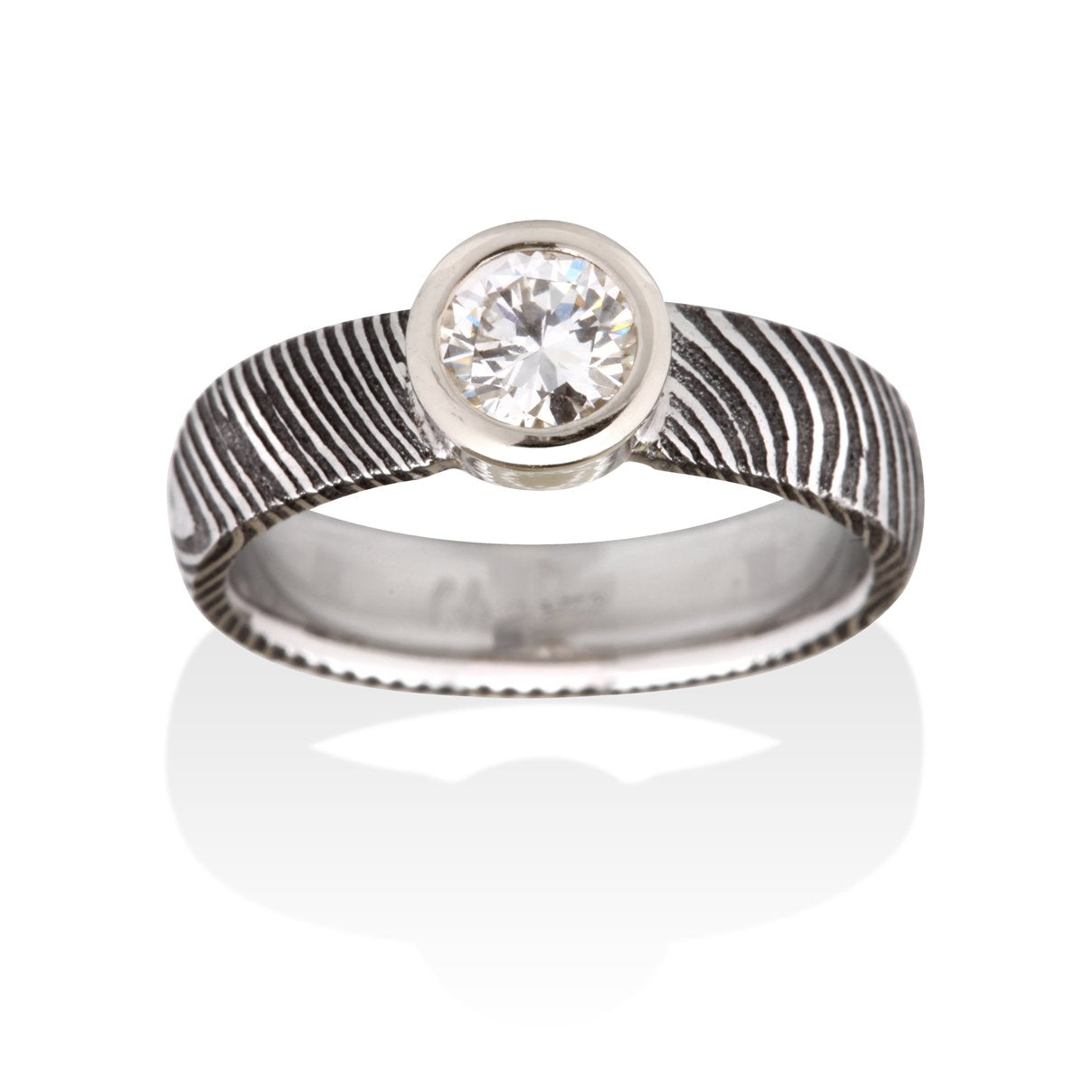 Silver ring with a round diamond and a Damascus steel band on a white background.
