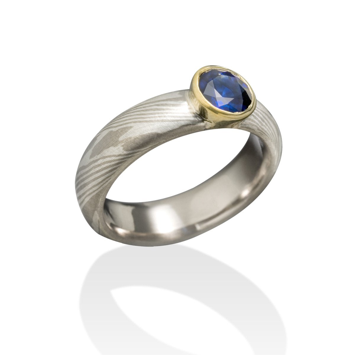 Silver gold ring with a round sapphire and a Damascus steel band on a white background.