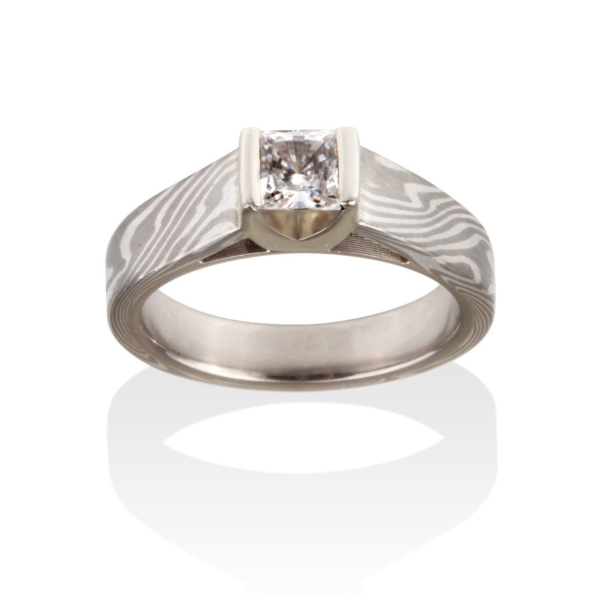 Silver ring with a princess-cut diamond and a Damascus steel band on a white background