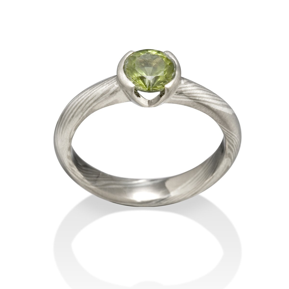 Silver ring with a round green gemstone and a Damascus steel band on a white background