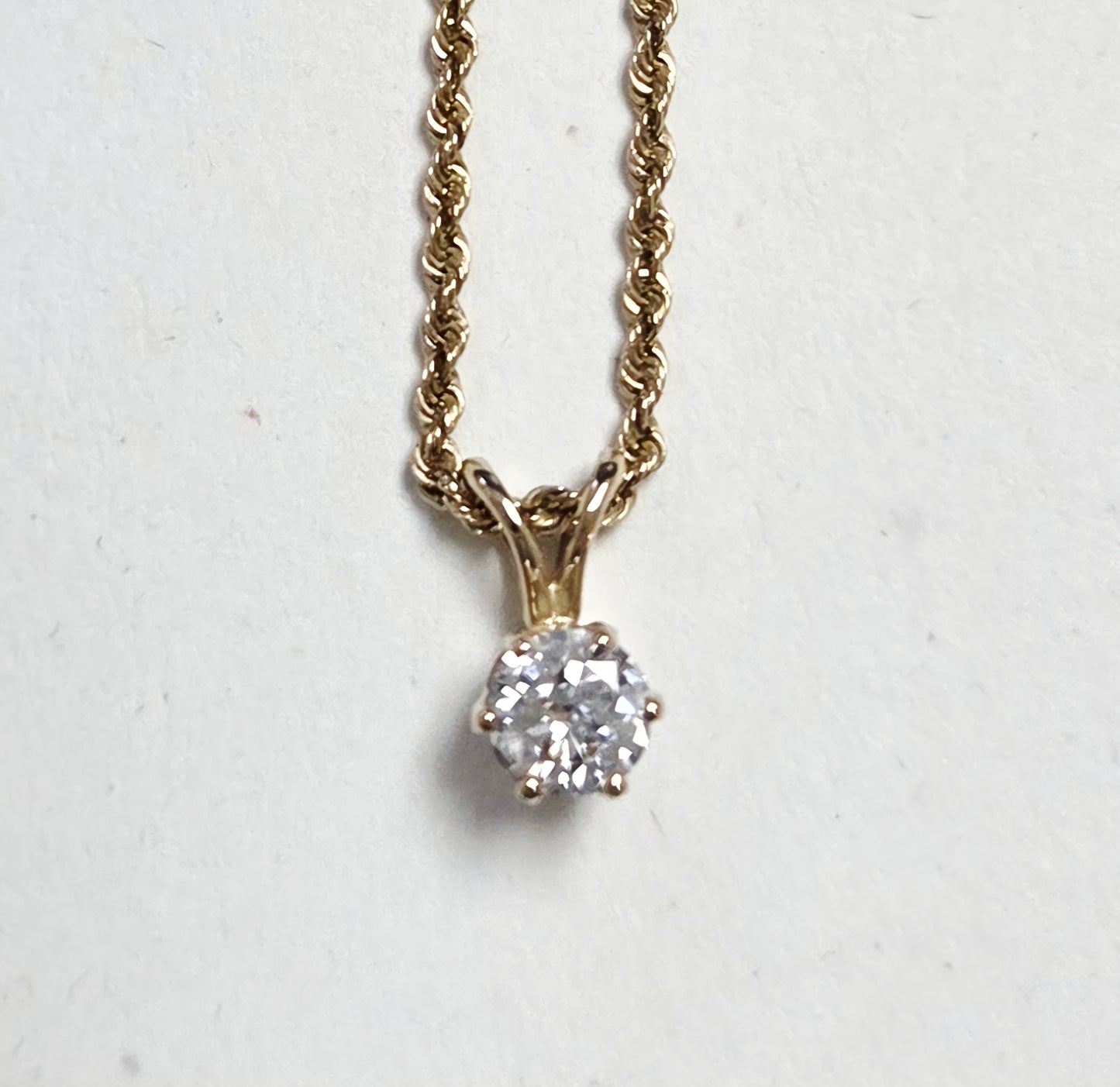 Gold necklace with a diamond pendant on a light gray background