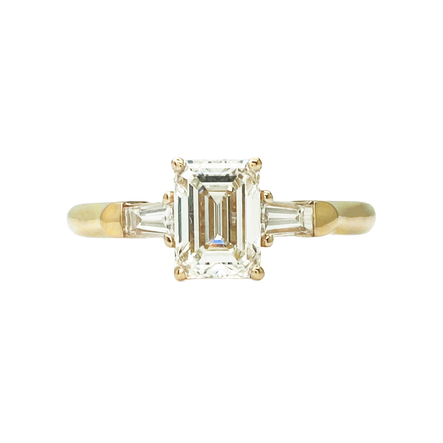 Gold ring with a central emerald-cut diamond and two side baguette diamonds on a white background