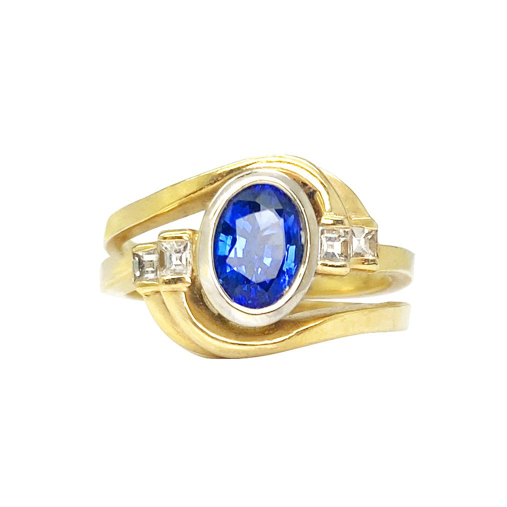 Gold ring with a blue sapphire stone set in a curved setting. The ring also features small diamonds on the sides. The background is white.
