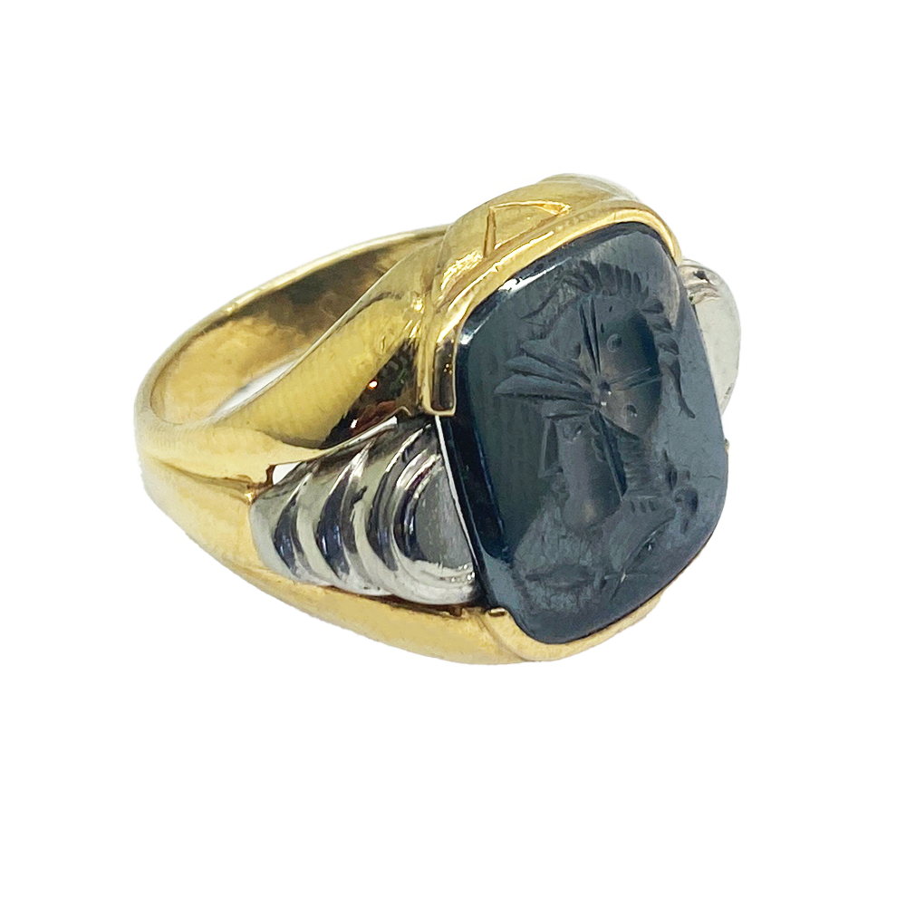 Vintage gold men's ring with a rectangular hematite intaglio featuring a detailed profile of a helmeted warrior. The ring has a textured gold band with a contrasting white metal inlay.