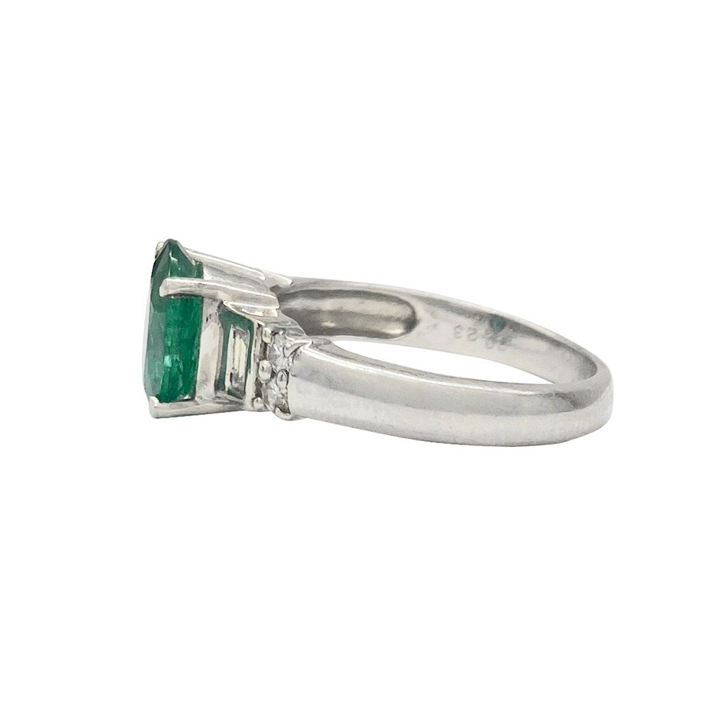 Silver ring featuring an oval emerald, flanked by two trapezoid-cut diamonds.