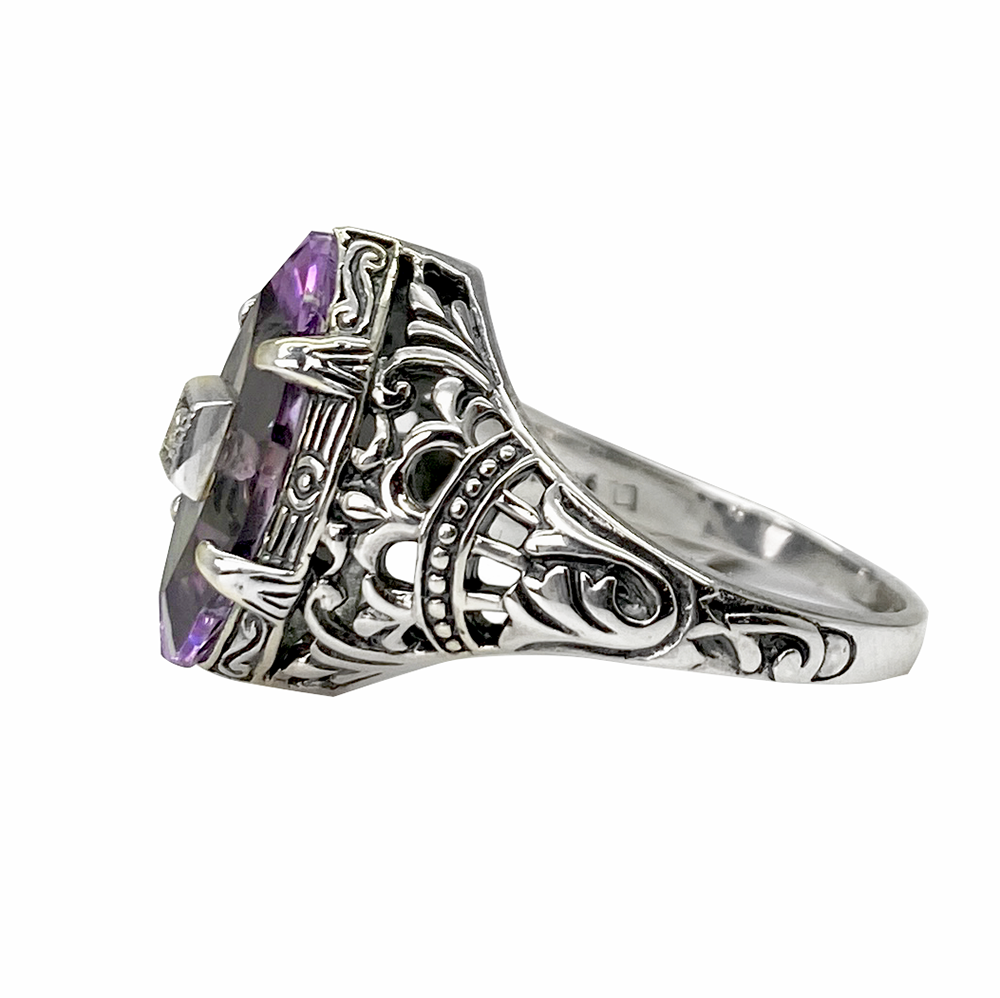 Sillver ring with a purple amethyst center stone and intricate filigree detailing, on a white background.