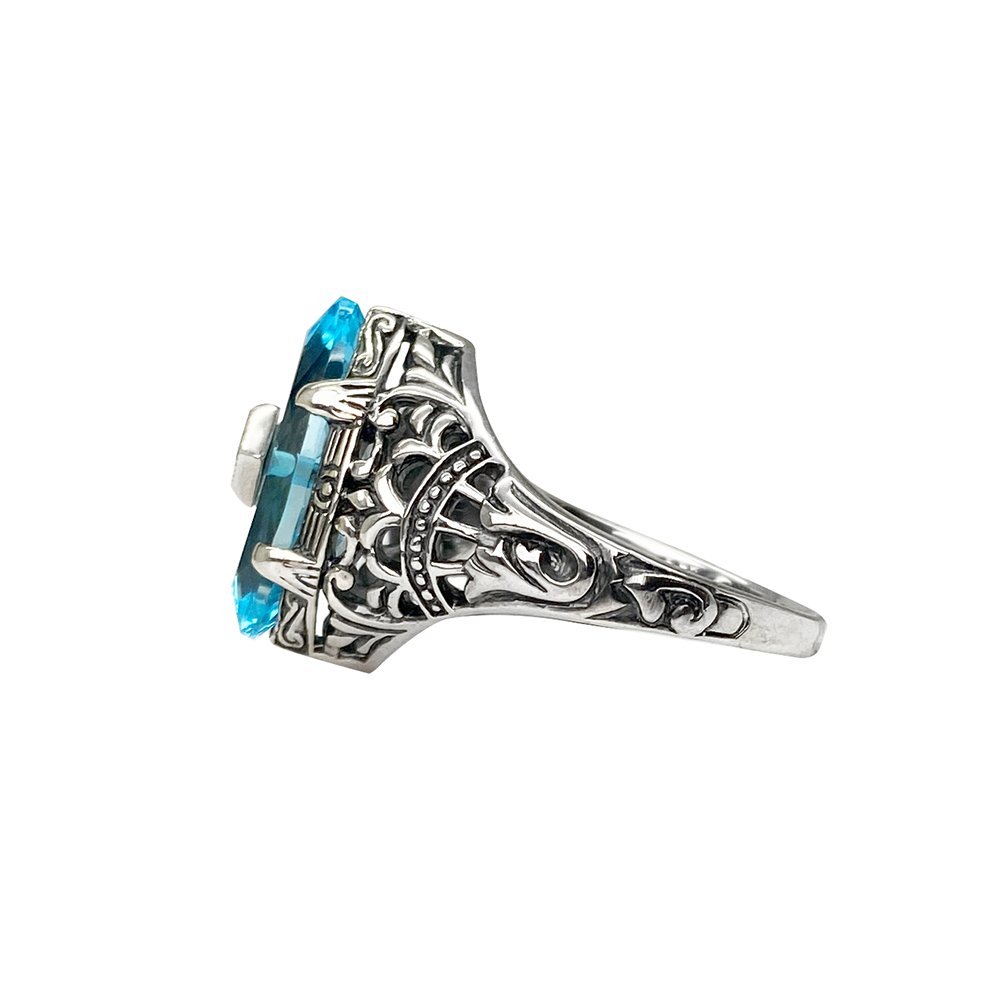 Silver ring with a blue topaz center stone and intricate filigree detailing, on a white background