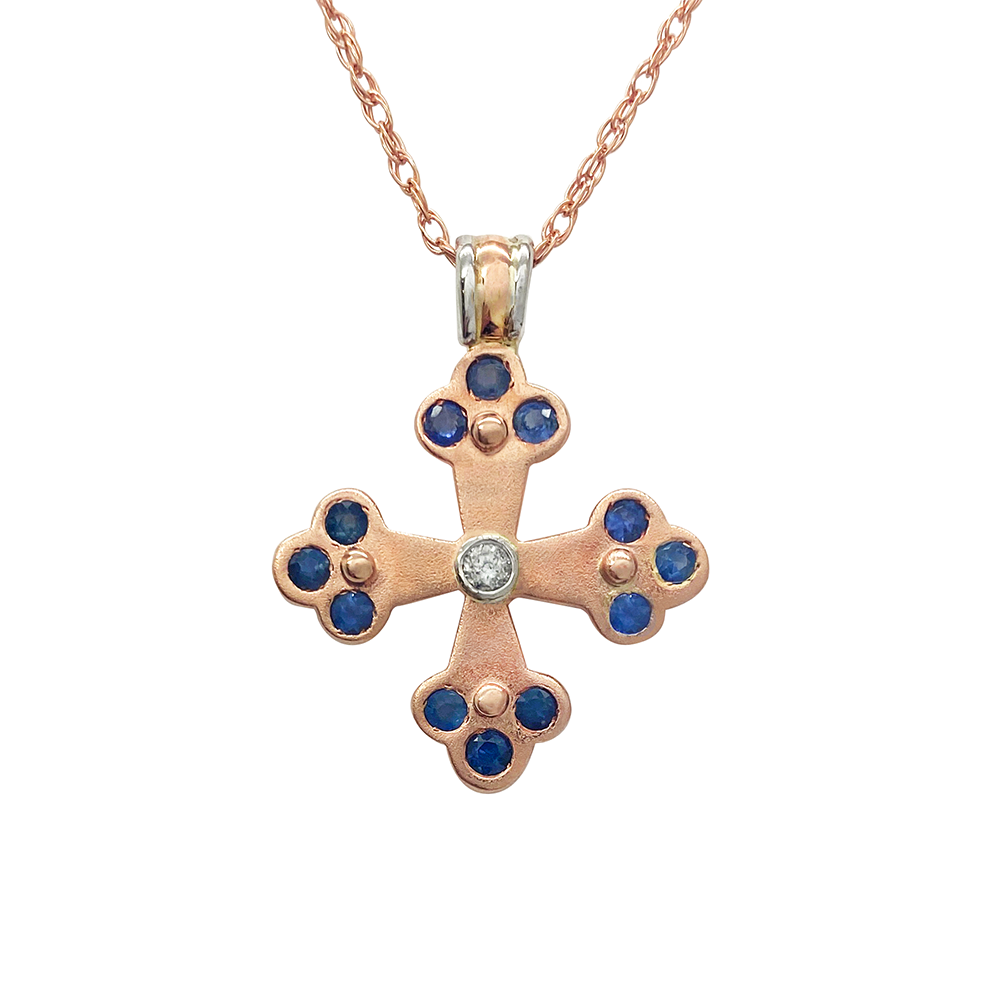Rose gold cross pendant with sapphires and a diamond in the center, on a white background.