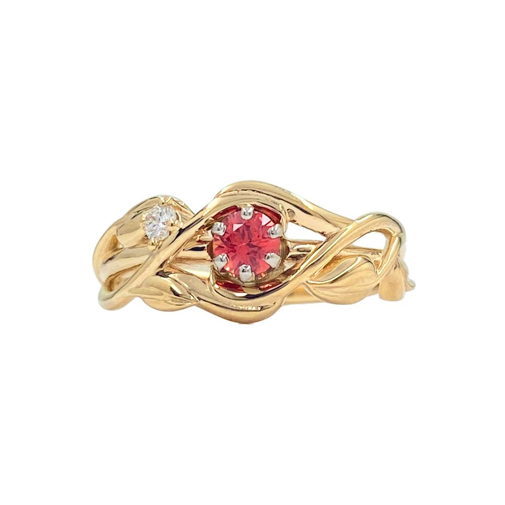 Gold ring with a flowing, intertwined bands that resemble branches. The ring holds a red center stone and a smaller white stone.