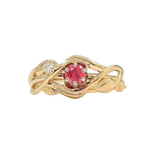 Gold ring with a flowing, intertwined bands that resemble branches. The ring holds a red center stone and a smaller white stone.