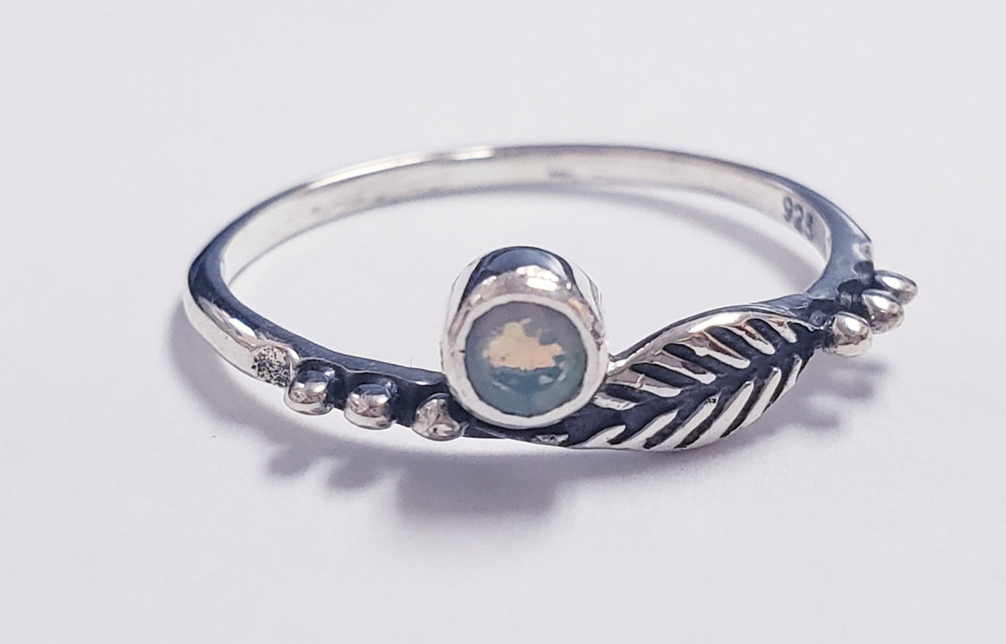 Silver ring with a opal gemstone and a leaf-shaped design on a white background.