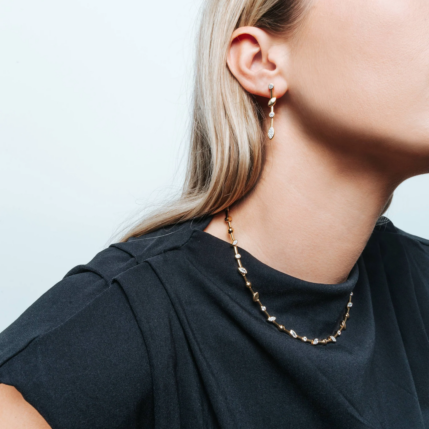 Close-up of a person wearing a gold necklace and earrings against a light background