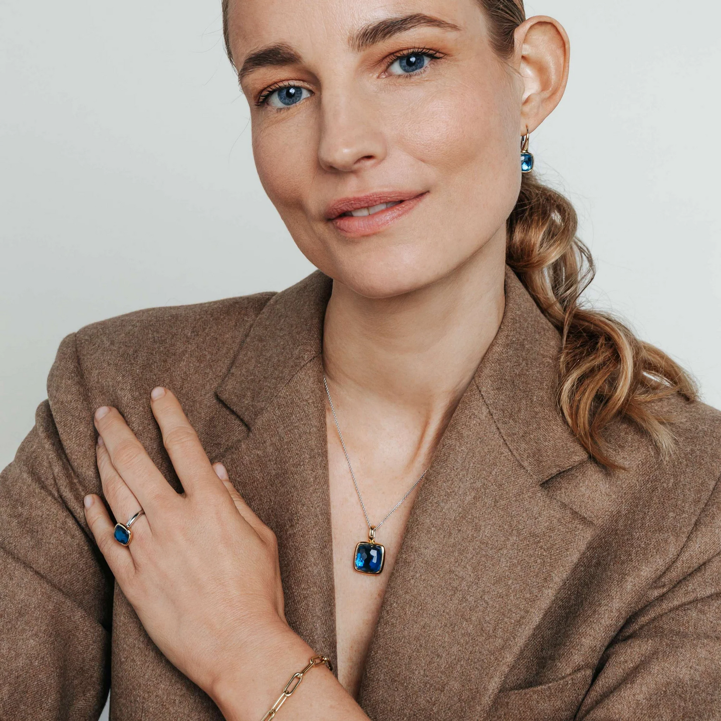 Woman wearing a brown blazer with jewelry, including earrings, ring, and necklace.