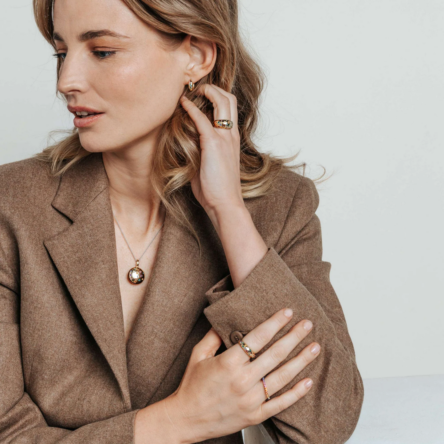 Woman wearing a brown blazer with jewelry on a plain background