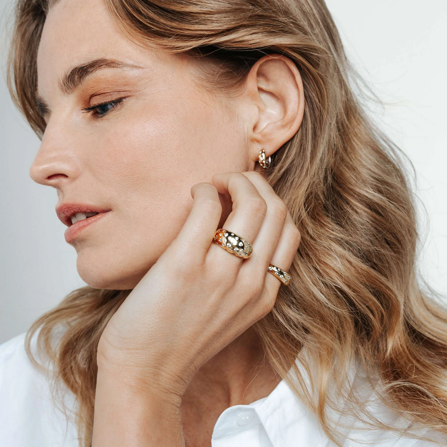 Woman wearing gold earrings and rings on a neutral background