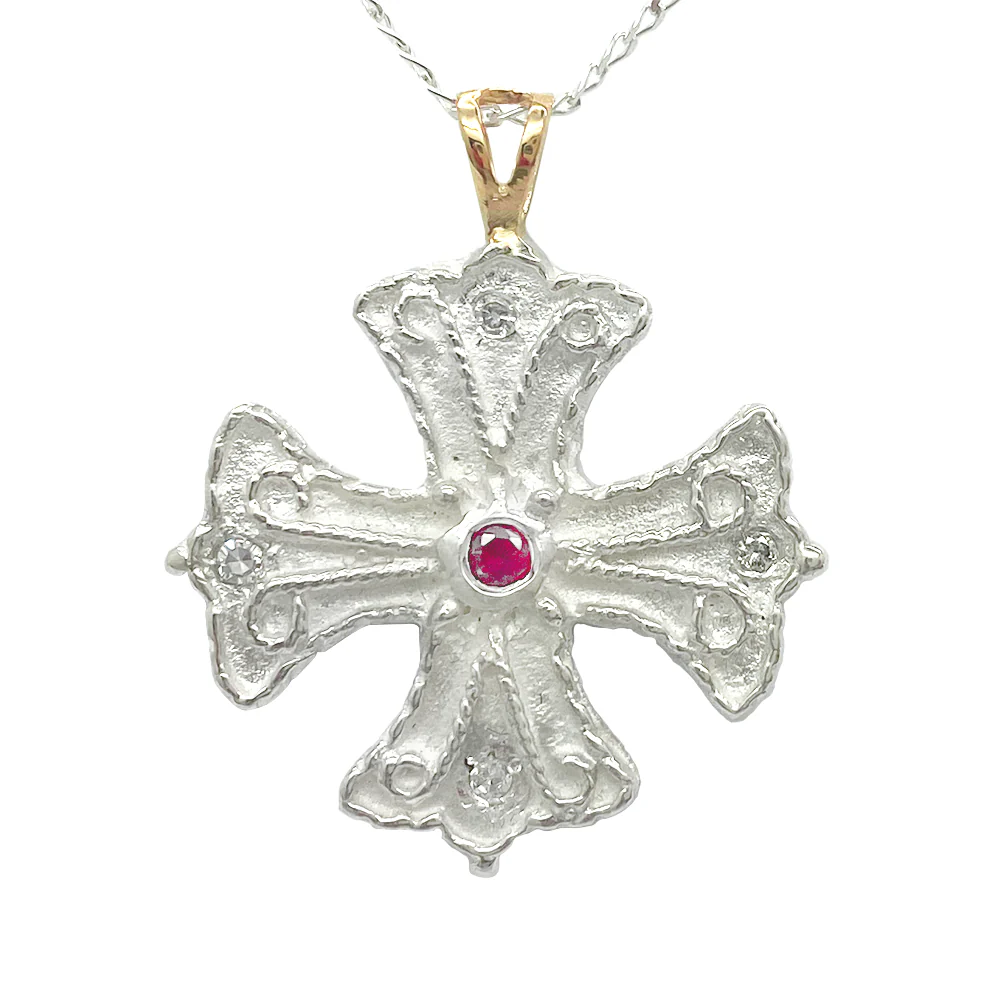 Silver cross pendant with a ruby center stone and diamond accents on a white background.