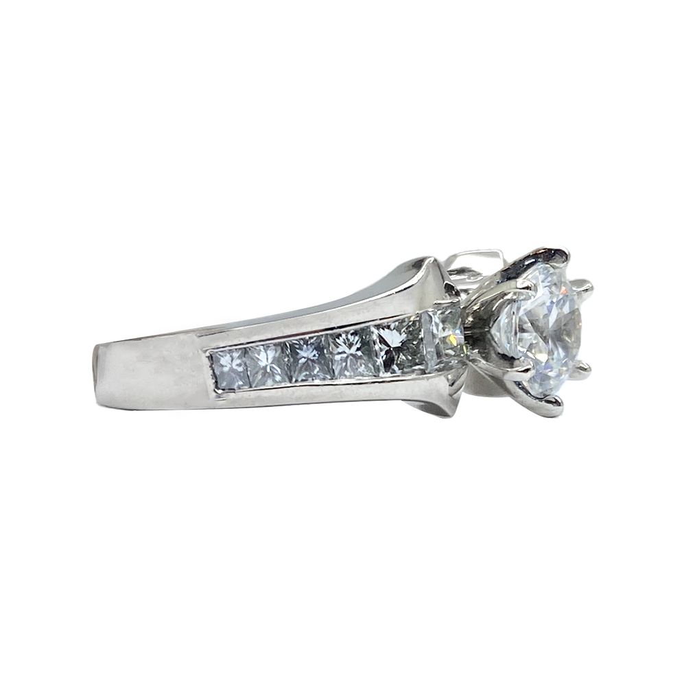 Silver engagement ring with a center round diamond flanked by two rows of round-cut diamonds on a shared prong setting.