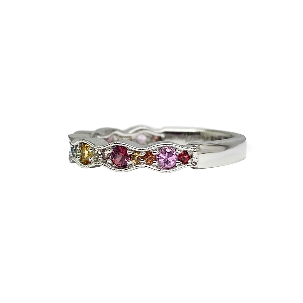 Side view of silver multi-gemstone ring with a wavy band featuring round sapphires in various colors including pink, purple, blue, yellow, and orange.