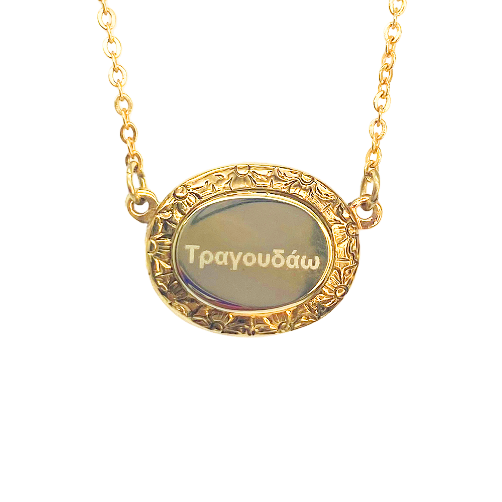 Gold oval pendant necklace with "Τραγουδάω" engraved in the center, surrounded by a floral border.