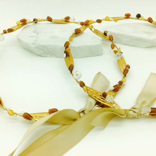 Pair of gold wedding crowns adorned with olive leaves and pearls, tied together with a white ribbon.