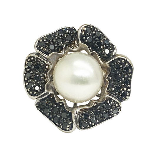 Silver flower-shaped ring with a large white pearl in the center and black diamond accents.