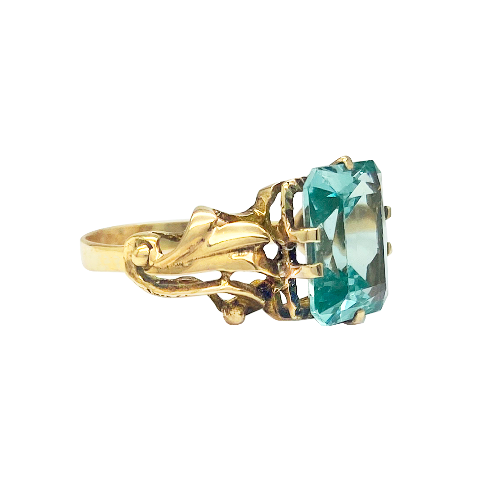 Gold ring with a blue topaz stone set in an Art Deco-style setting. Side view