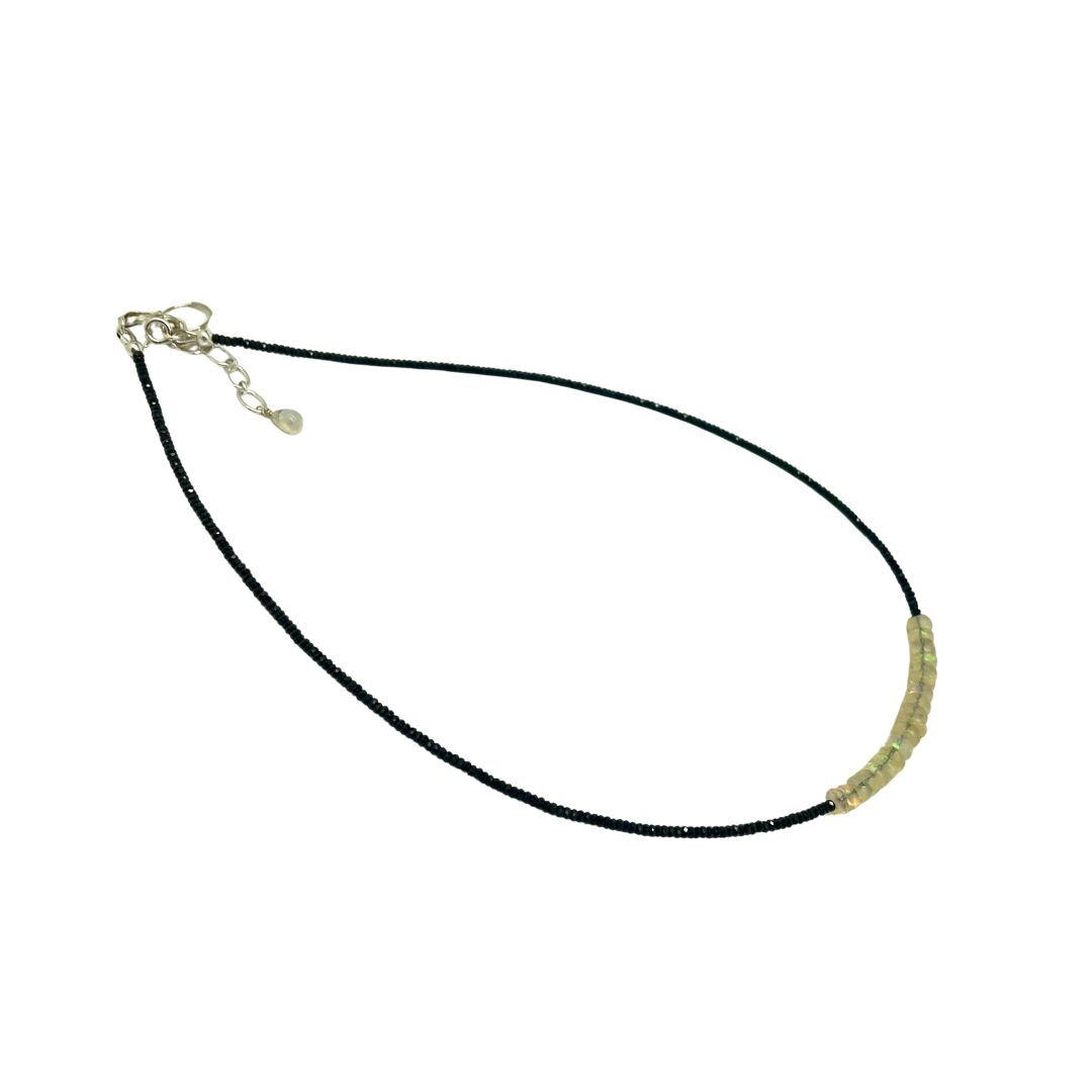 Black cord necklace with small gold beads on a white background