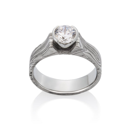 Silver ring with an oval diamond and a Damascus steel band on a white background