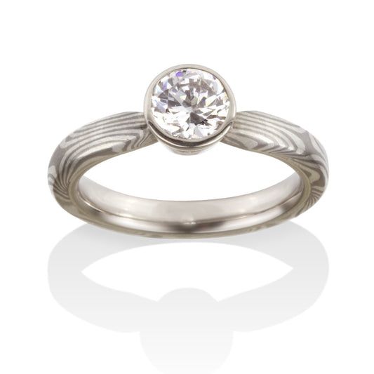 Titanium ring with a round diamond and a Damascus steel band on a white background.