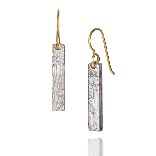 Pair of gold earrings with a damascus steel pattern, on a white background.