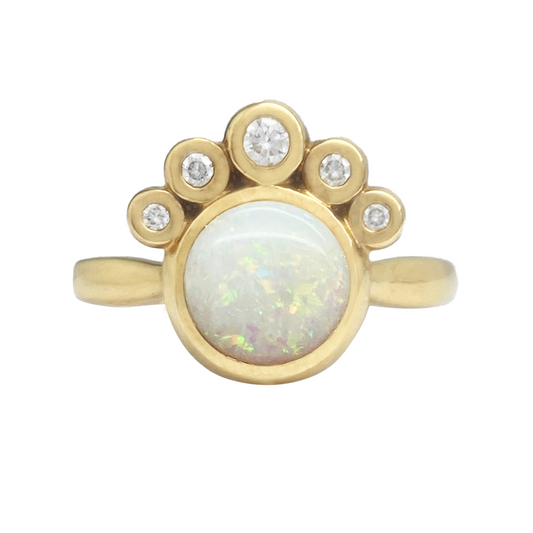 Gold ring featuring an oval opal surrounded by a cluster of five round diamonds. 