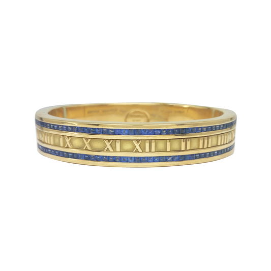 Gold ring with blue gemstones and Roman numeral design on a white background