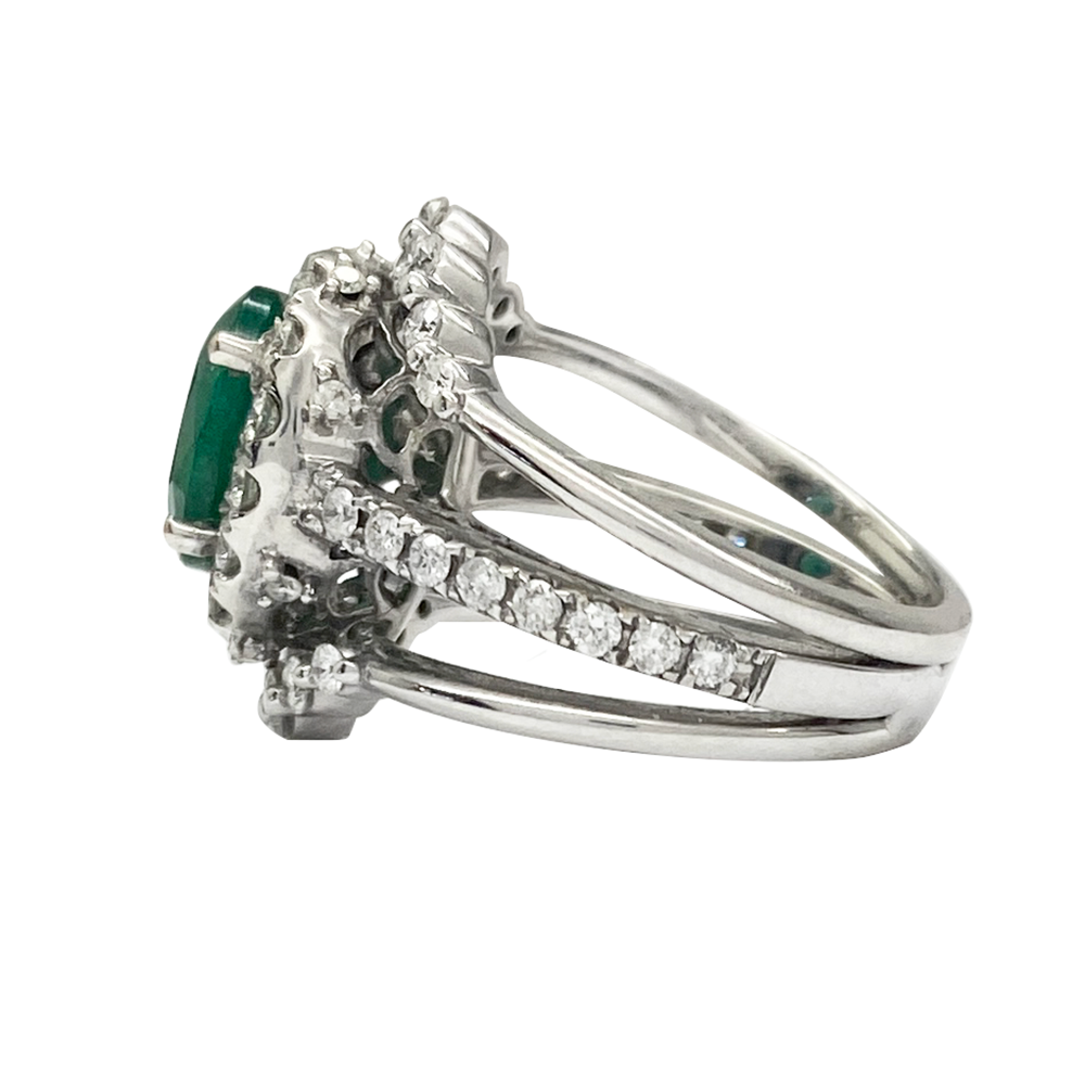 Silver ring with an oval emerald surrounded by a halo of round diamonds. The ring features a split shank with diamond accents.
