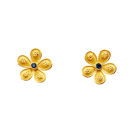 Gold flower-shaped stud earrings with blue sapphire centers, on a white background