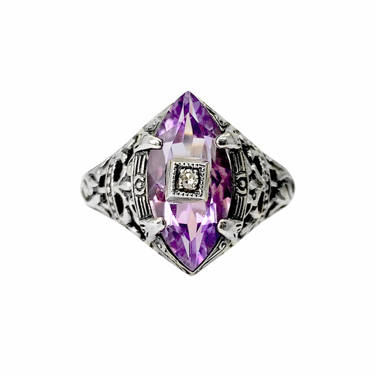 Sillver ring with a purple amethyst center stone and intricate filigree detailing, on a white background.