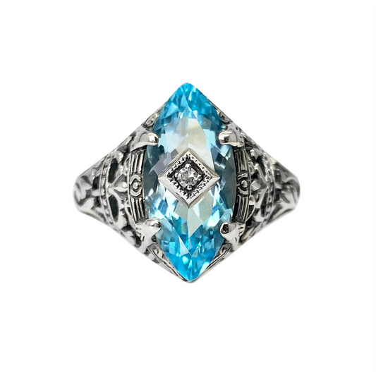 Silver ring with a blue topaz center stone and intricate filigree detailing, on a white background