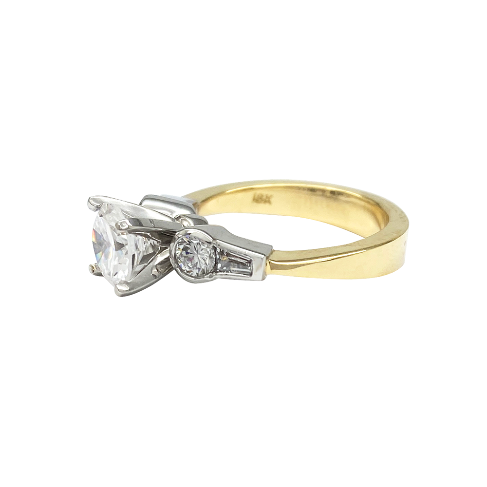 Yellow gold engagement ring with a round diamond center stone and baguette-cut side stones, on a white background.
