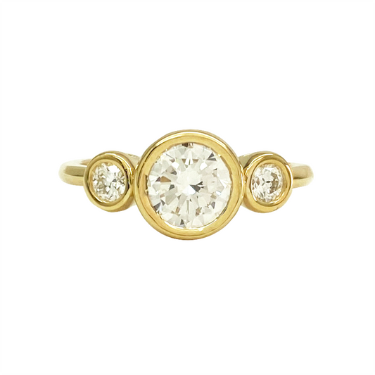 Yellow gold ring with three round diamonds in a bezel setting on a white background