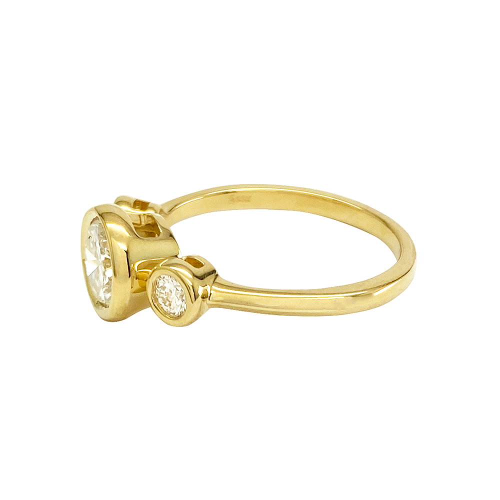 Yellow gold ring with three round diamonds in a bezel setting on a white background