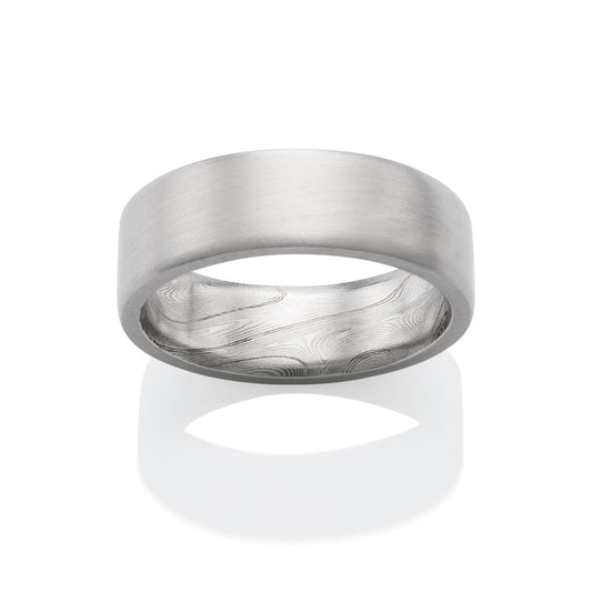 Stainless steel ring with a Damascus steel pattern on the inside, on a white background.