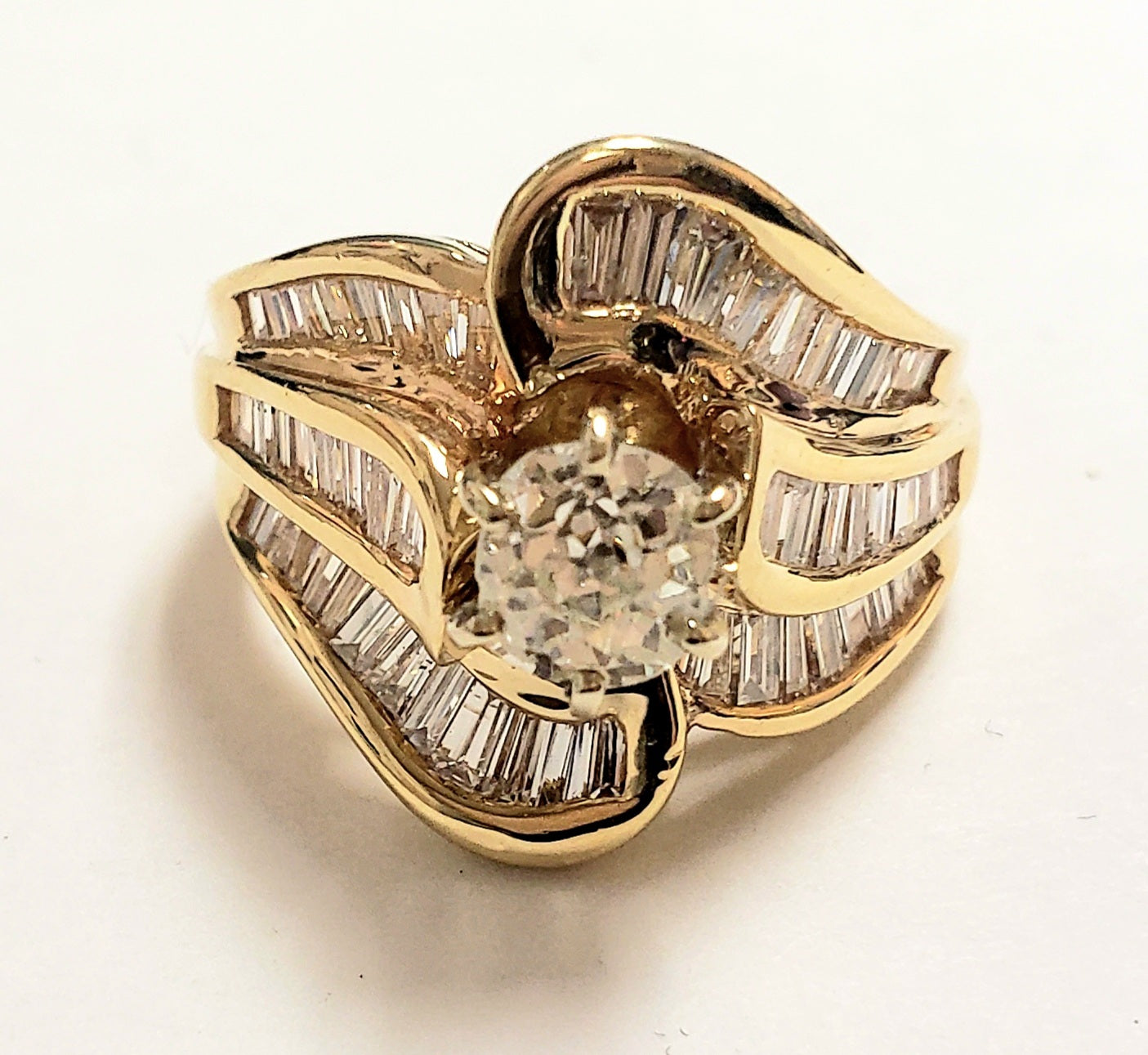 Yellow gold ring with a round diamond in the center, surrounded by baguette diamonds.